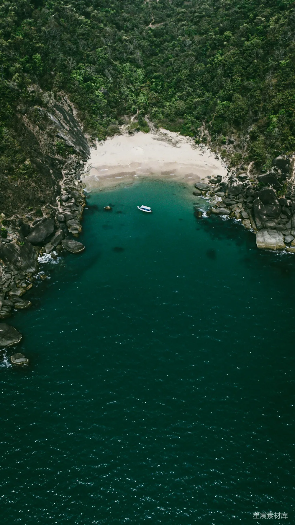 这张航拍照片捕捉到了一个宁静的海湾，清澈的海水与周围的绿色植被形成了鲜明的对比。在海湾中，有一艘孤舟静静地漂浮着，增添了一丝悠然自得的氛围。这种场景非常适合用于旅游宣传或自然风光展示。