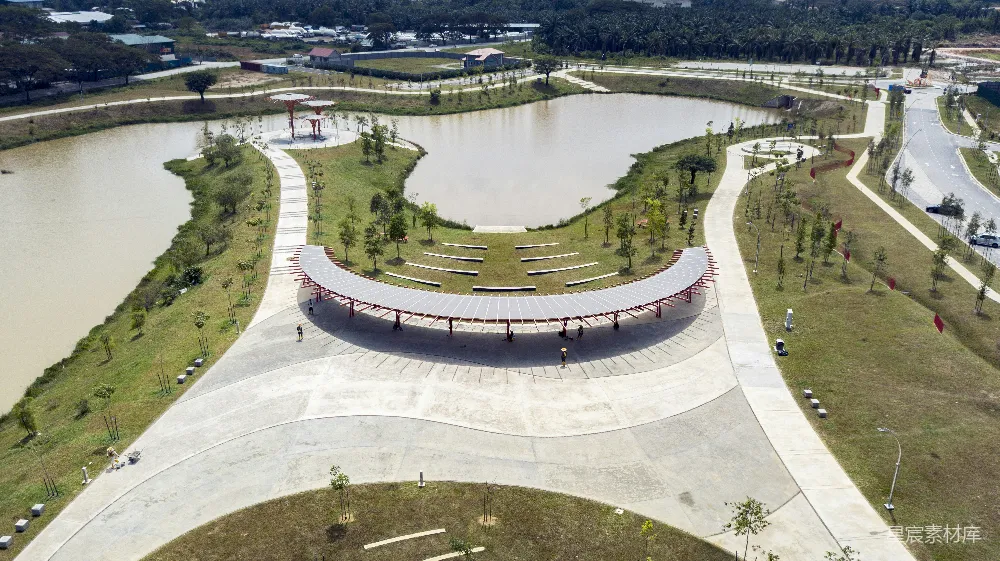 这张航拍图展示了一个现代化的公园景观，中央有一个弧形的凉亭，周围是蜿蜒的小路和树木，远处有一片水域。整个场景设计简洁明快，适合休闲娱乐和放松心情。