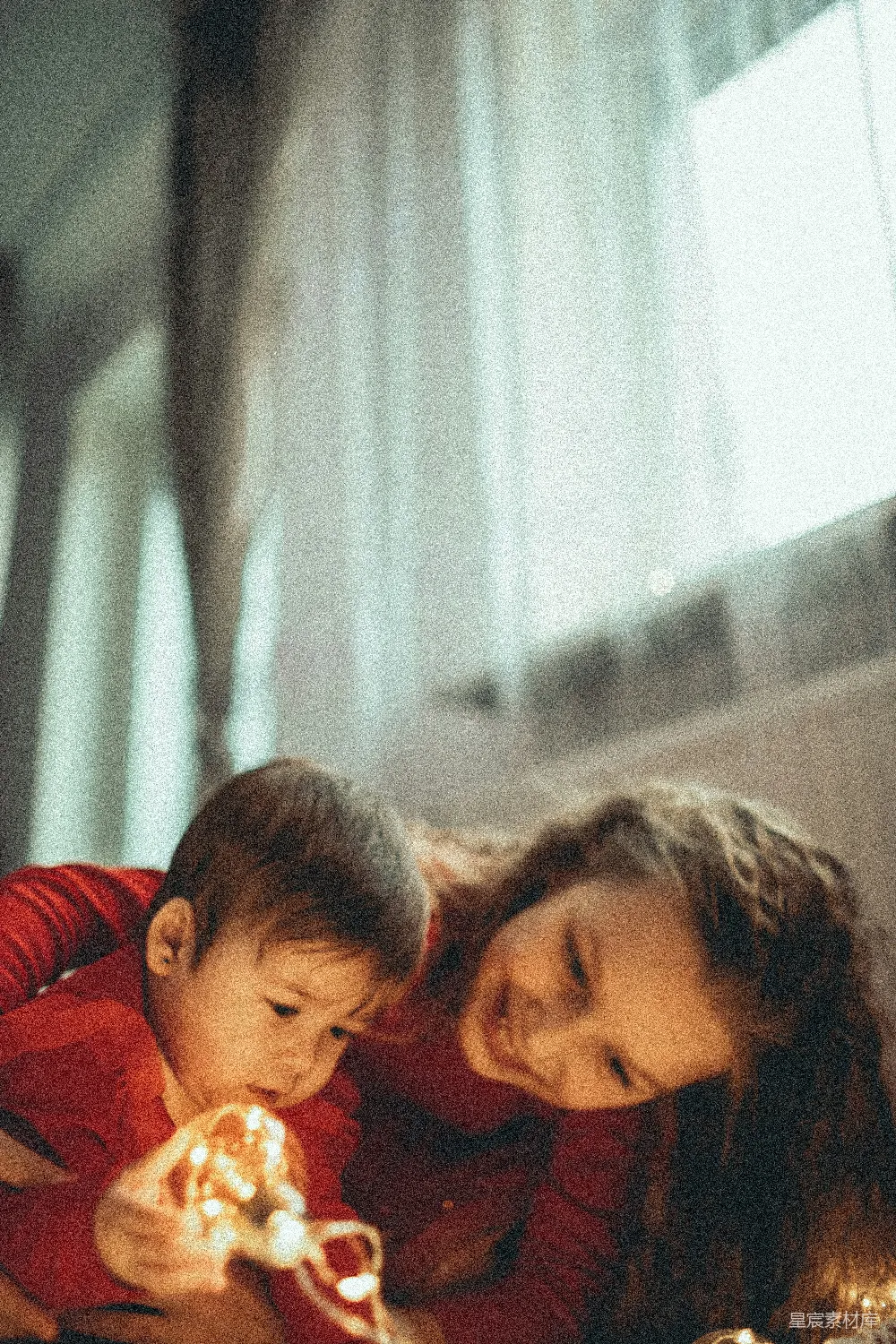 图片中，一位母亲和她的儿子在一起，母亲温柔地依偎着儿子，儿子手里拿着一串温暖的灯饰，两人共同享受着温馨的时光。这种场景适合用于展现家庭的幸福与爱，适合用作家庭生活、亲子教育或温馨主题的背景素材。