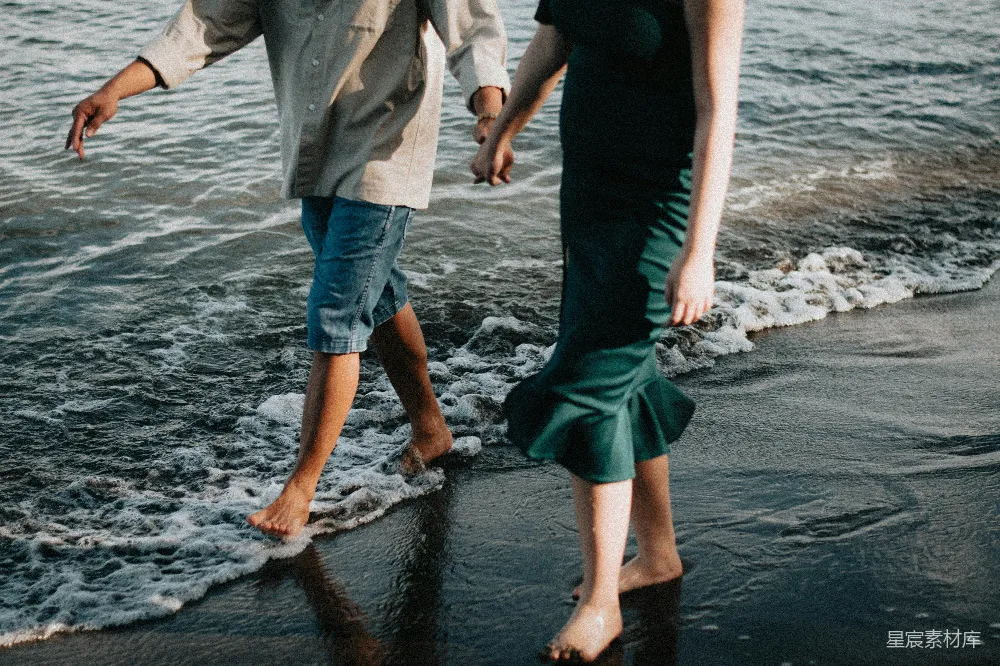 一对男女手牵手在海滩上漫步，海水轻拍着脚踝。他们的身影在夕阳的余晖中显得格外温馨浪漫，展现了简单而美好的爱情。适合用作爱情故事、自然风光或休闲时光的背景图。