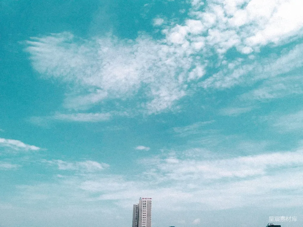 图片展示了一片蓝天下的城市景象，天空中散布着几朵白云，显得格外清新。地平线处有一栋现代化的高楼建筑，远处的建筑轮廓在蓝天白云的映衬下显得格外清晰。这张照片给人一种宁静而放松的感觉，适合用于背景图或城市宣传图片。