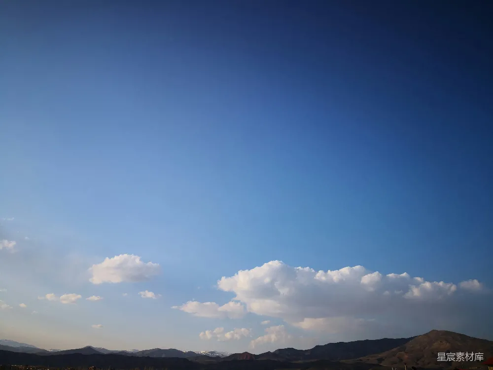 这张图片展示了一片蓝天背景下，几朵白云漂浮在天空中，山峦起伏，景色宁静而美丽。适合用作自然风光的背景图片，或用于表达宁静、平和的情感。