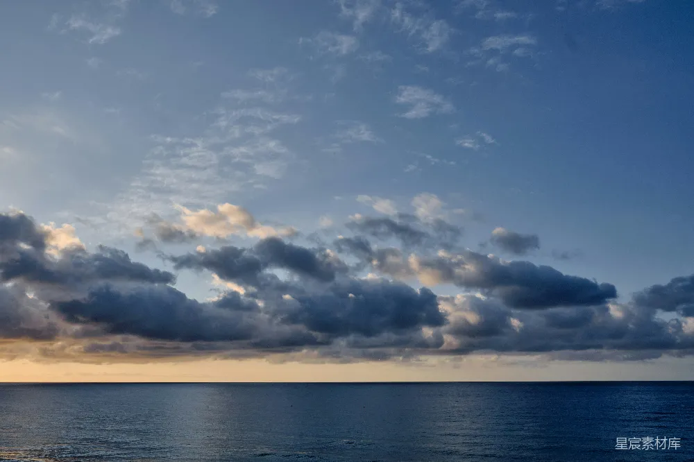 这张图片展示了一幅宁静的海景，天空中散布着几朵云彩，阳光洒在云层上，反射出温暖的光芒。海面平静如镜，与天空的颜色融为一体，营造出一种宁静祥和的氛围。适合用作自然风光、旅行摄影或静谧场景的背景图。