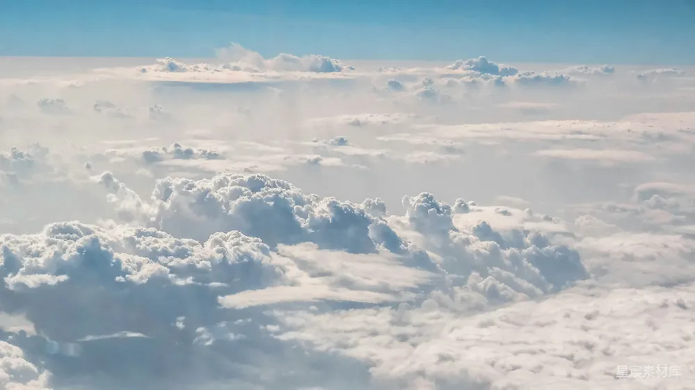 这张图片展示了从高空中俯瞰的壮观云海景象。天空呈现出淡蓝色，云层厚实，形态各异，给人一种宁静而神秘的感觉。这样的画面适合用于旅行、自然风光、放松心情等场景。