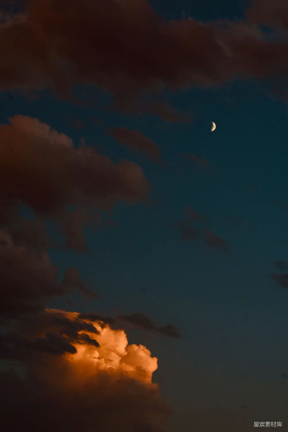 这张图片展示了夜空中的一弯新月，背景是被夕阳染成橙色的云层，天空呈现出深邃的蓝色。新月与云层的结合营造出一种宁静而神秘的氛围，适合用作自然风光、宁静夜晚或浪漫主题的背景素材。