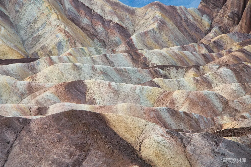 这张图片展示了沙漠中色彩斑斓的地貌，层层叠叠的山丘呈现出丰富的色块，仿佛是一幅自然的大地之毯。这种地貌通常出现在干旱地区，由风化和沉积作用形成，给人以强烈的视觉冲击和自然的壮丽感。适合用于自然景观、地质学研究或旅游宣传。