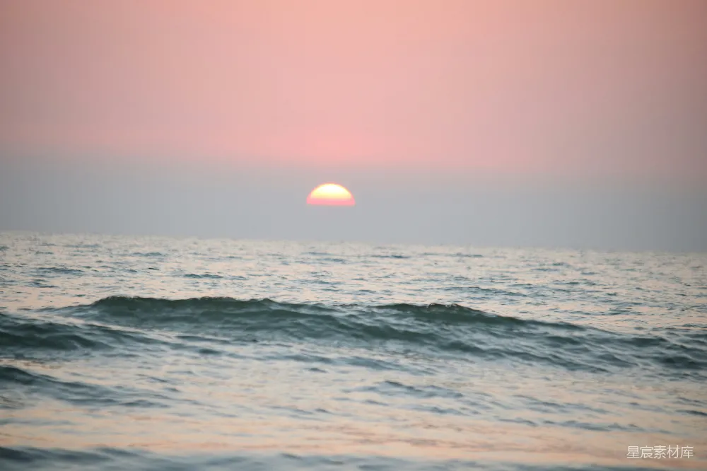 这张图片展示了一幅宁静的海景，夕阳的余晖洒在波光粼粼的海面上，天空被染成了柔和的粉红色。海水的波纹细腻，给人一种平静而深邃的感觉。适合用作自然风光、旅行记、放松心情的背景素材。