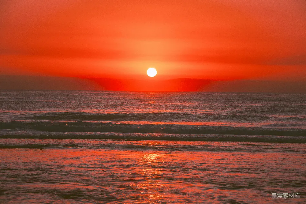 夕阳的余晖洒在波光粼粼的海面上，金色的光晕与红色的天空交相辉映，海浪轻轻拍打着沙滩，展现出一种宁静而美丽的自然景观。
