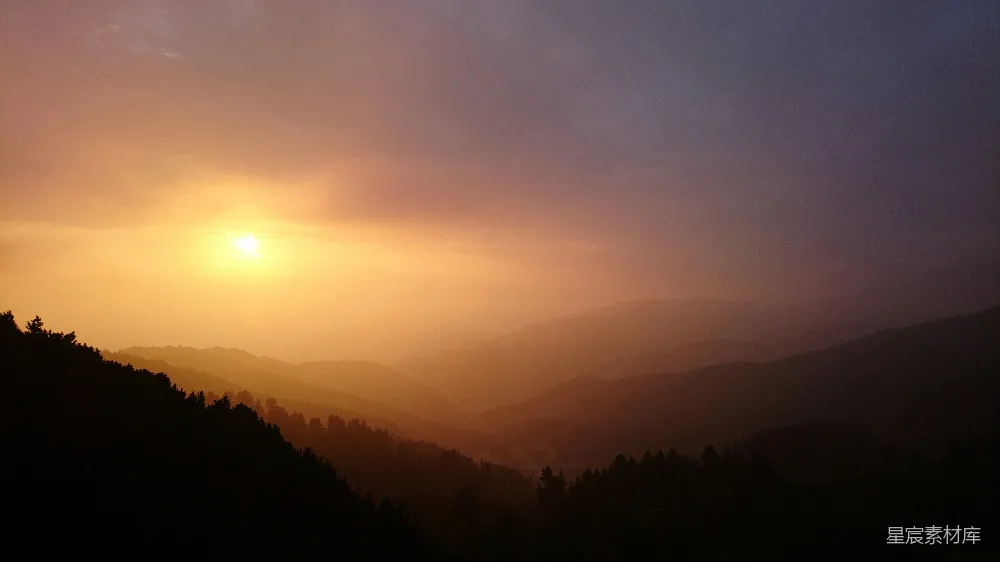 夕阳的余晖洒在连绵起伏的山谷上，山峦的轮廓在夕阳的映衬下显得格外清晰。天空中淡淡的云彩与地平线上的落日相接，营造出一种宁静而壮丽的自然景象。这幅画面适合用作自然风光的背景或静谧心灵的视觉元素。