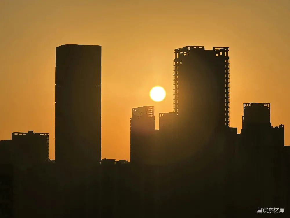 这张图片展示了夕阳时分的城市剪影，金黄色的阳光从高楼大厦的间隙中透出，形成了鲜明的对比。天空被染成了温暖的橙色，城市的轮廓在夕阳的光辉中显得更加清晰。这幅画面适合用于城市风光、自然风光和日落主题的背景或海报设计。