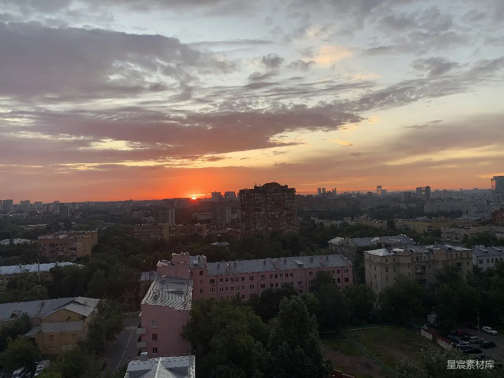 这张图片展示了一个城市中的日落景象，天空被橙色和粉色的晚霞染色，建筑物的轮廓在落日的余晖中显得格外清晰。树木和屋顶在前景中形成了自然与人工建筑的对比，营造出一种宁静而美丽的氛围。适合用作城市生活的背景图片，或是表达自然美景与城市生活和谐共存