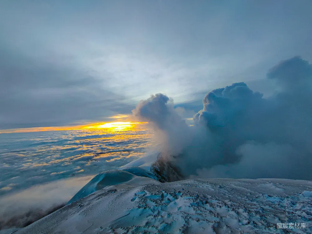 这张图片展示了火山爆发与日出的壮丽景象。火山口喷发出的浓烟与火山灰在空中弥漫，与下方的云层交织在一起，形成了壮观的视觉效果。太阳在地平线上方升起，金色的光芒穿透云层，照亮了火山口和周围的雪地。这种场景不仅展现了大自然的壮观，也让人感受到大自