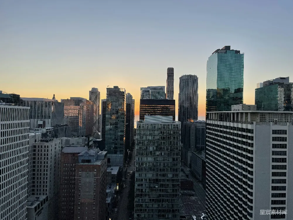 这张图片展示了城市日落时的天际线，高楼大厦在夕阳的映衬下显得格外壮观。天空从橙黄色渐变至深蓝色，与城市的建筑形成鲜明对比，给人一种宁静而优雅的感觉。适合用作城市风光、都市生活或自然与建筑结合的背景素材。