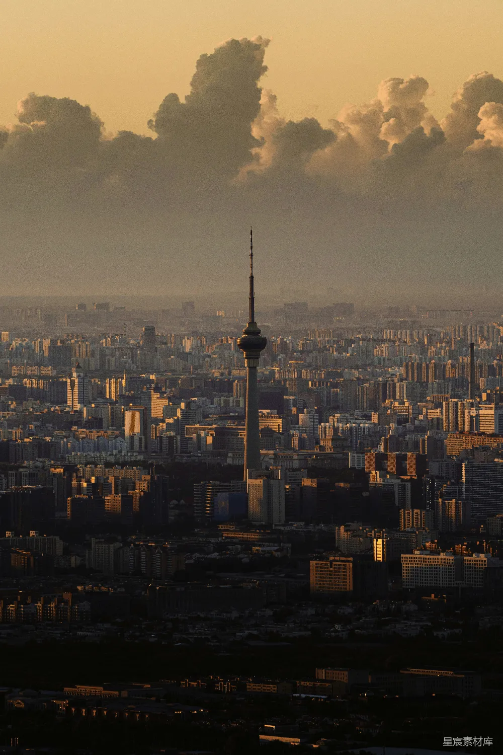 这张图片展示了日落时分的城市全景。画面中央是一座高大的塔楼，背景中散布着许多低矮的建筑物，远处的天空被夕阳染成了金黄色，云层在阳光的照射下显得格外壮观。整个场景给人一种宁静而美丽的感觉，适合用作城市风光或日落主题的背景图片。