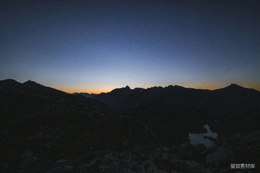 在这张图片中，夕阳的余晖洒在山峦和湖面上，形成了美丽的渐变色。山峰的轮廓在昏暗的天空中显得格外清晰，而湖水则在夕阳的映照下展现出深邃的蓝绿色。整个场景宁静而美丽，给人一种平静和放松的感觉。