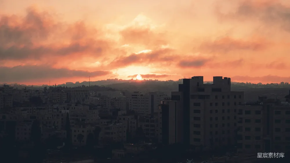 这张图片展示了城市日落时的宁静与美丽。夕阳在地平线上缓缓落下，天空被染成橙红色，云层在夕阳的映照下显得格外壮观。城市的轮廓在夕阳的余晖中若隐若现，形成了一幅剪影效果。这样的场景适合用作城市风光或日落主题的背景图片。
