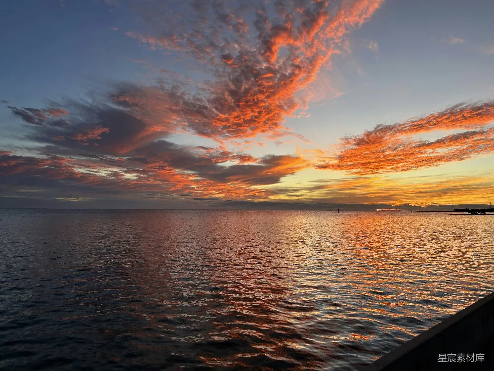 这张图片展示了一幅宁静美丽的夕阳景象，天空被染成了橙红色，海面反射出这些色彩，波光粼粼。整体画面给人一种宁静与祥和的感觉，非常适合用作旅行或自然风光的背景素材。