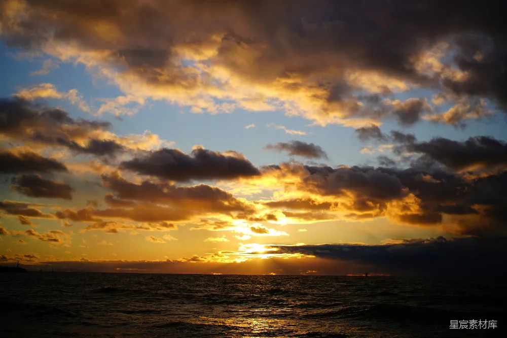 这张图片展示了金色的海平线，夕阳的余晖洒在云层和海面上，形成美丽的光影效果。天空中散布着几朵云彩，反射出温暖的光芒，给人一种宁静而祥和的感觉。适合用作自然风光或旅行摄影的背景图。