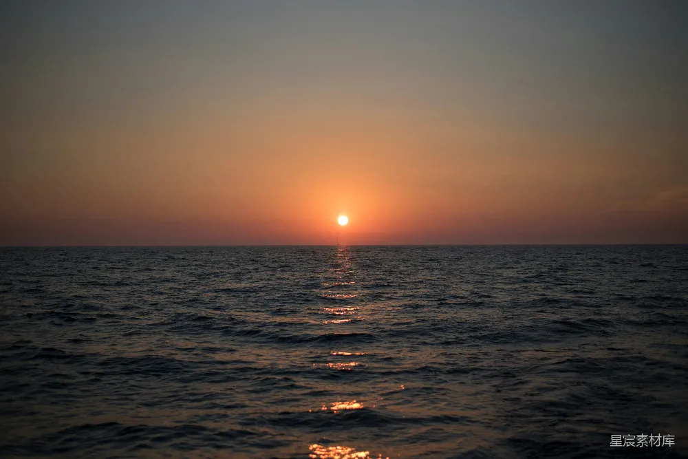 图片展示了一幅美丽的夕阳海景，太阳缓缓沉入海平线，金色的光芒在海面上洒下斑驳的光影。海面平静而深邃，天空从橙黄渐变至深蓝，营造出一种宁静而壮丽的氛围。适合用于表达宁静、自然与美好时光的主题。