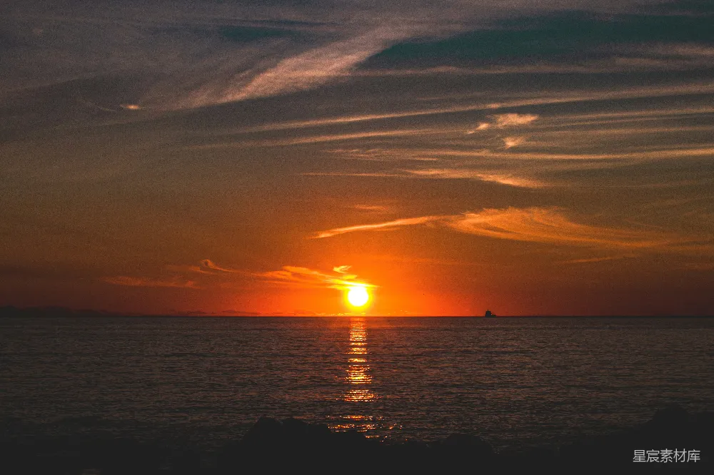 这是一幅宁静的夕阳海景图。夕阳的余晖洒在海面上，形成美丽的橙色和金色光晕。天空中飘着几缕云彩，反射在水面上，增添了画面的层次感。远处有一艘小船，与广阔的海面形成对比。整体画面给人一种平静、祥和的感觉，适合用作旅行、自然风光的背景图片。