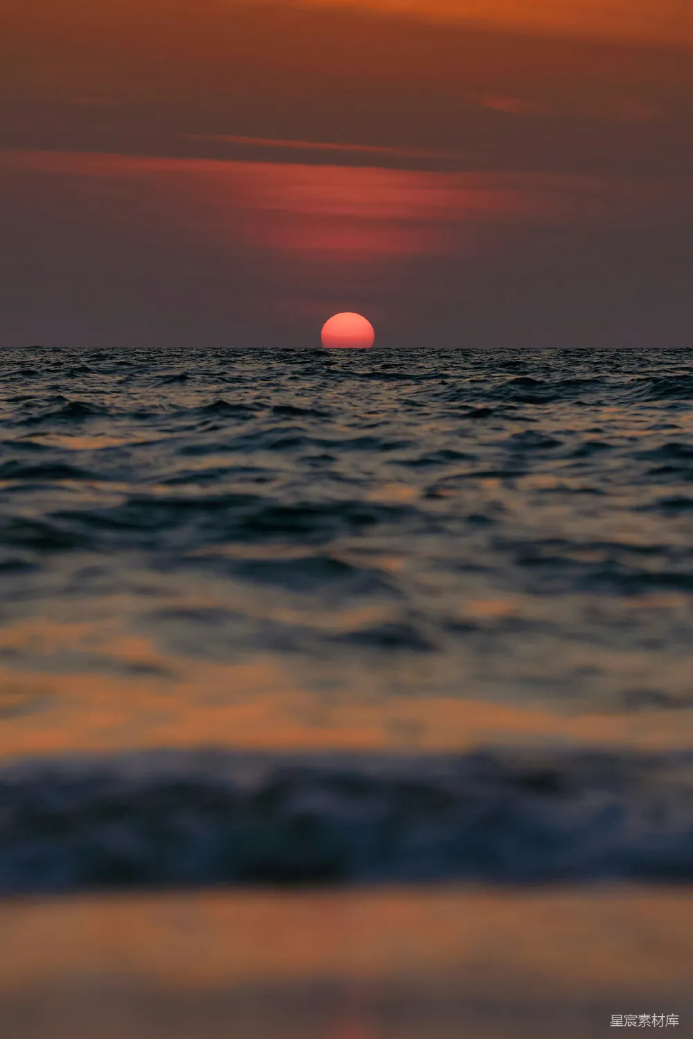这张图片展示了一个宁静的日落场景，太阳正缓缓沉入海平线。天空被染成了温暖的橙红色，海面波光粼粼，反射着夕阳的余晖。这种场景非常适合用来表达平静与宁静，或是作为自然风光的背景。