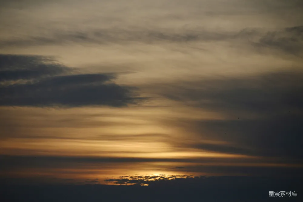 黄昏时分，天空被夕阳染成橙黄色，云层在夕阳的映照下呈现出柔和的色调，给人一种宁静而美好的感觉。这种场景适合用作自然风光、日落或宁静氛围的背景素材。