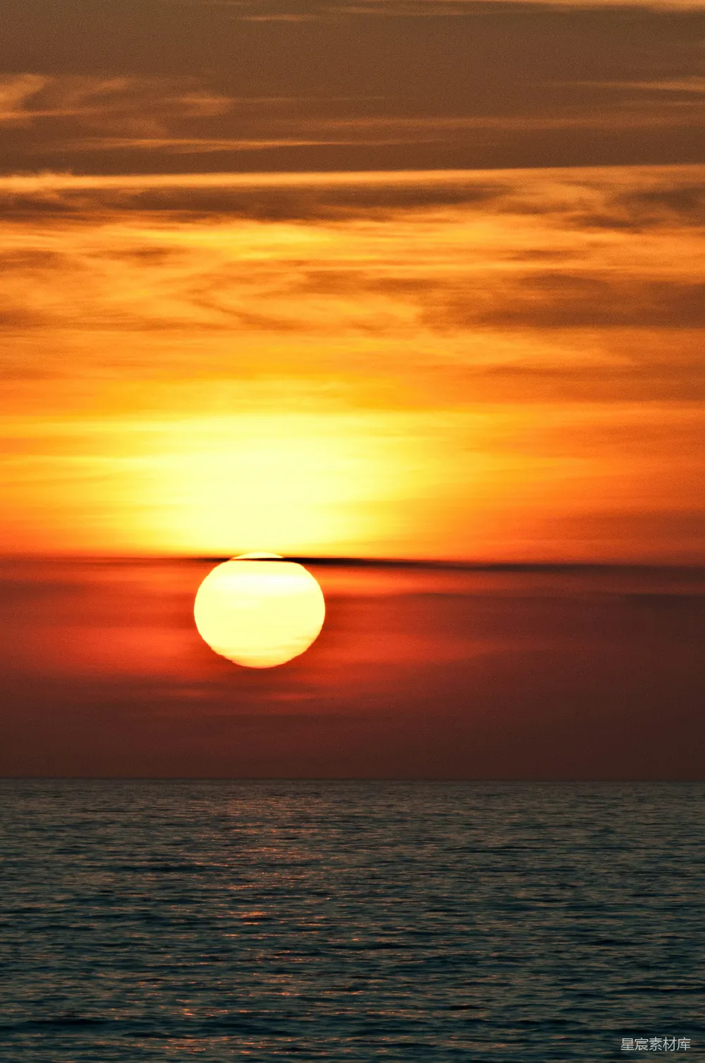 这张图片展示了一个宁静的日落场景，太阳缓缓落入海平线，天空被染成了美丽的橙色和红色。海面波光粼粼，反射着夕阳的余晖，给人一种宁静与平和的感觉。适合用作自然风光、旅行摄影或静谧时刻的背景。