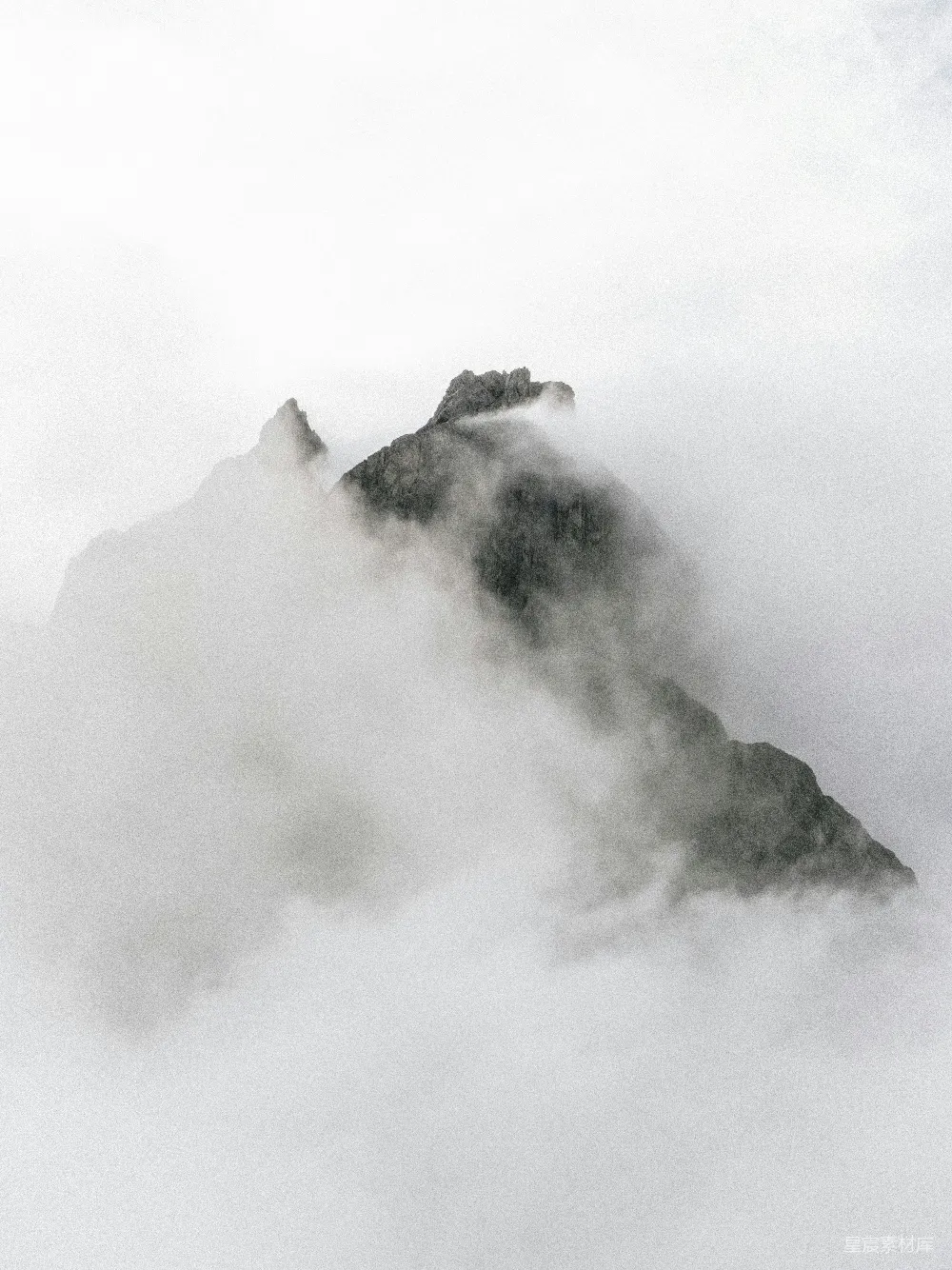 这张黑白照片展示了山峰在云海中的景象，山峰的轮廓在云雾中若隐若现，给人一种宁静而神秘的感觉。这种场景适合用于自然风光、旅行和探险主题的背景图。