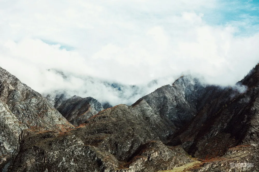 这张图片展示了一片云雾缭绕的山间景色，山峰在云雾中若隐若现，给人一种神秘而宁静的感觉。山体的纹理清晰可见，呈现出一种自然的美感。适合用于展示自然风光、户外探险或旅行主题的场景。