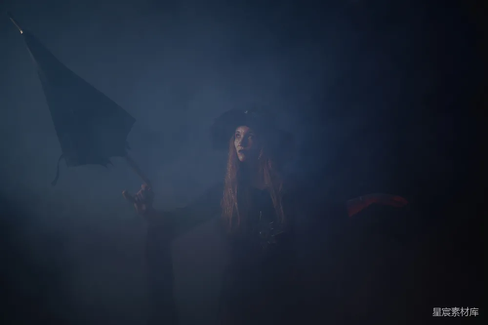 图片中，一位女巫在浓雾中挥舞着魔杖，背景是深邃的夜色，营造出一种神秘而诡异的氛围。女巫的神情专注，似乎正在施法，手中的魔杖在雾气中若隐若现，增添了画面的神秘感。这幅图像适合用于万圣节主题、神秘故事或奇幻场景的背景。
