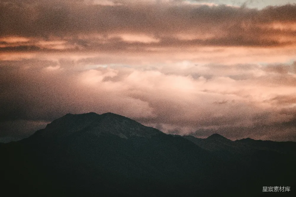 这张图片展示了一幅宁静的山景，山峦在夕阳的余晖下显得轮廓分明，云海缭绕，天空被染成了橙色和紫色的渐变色调，营造出一种宁静而神秘的氛围，适合用作自然风光或旅行主题的背景素材。