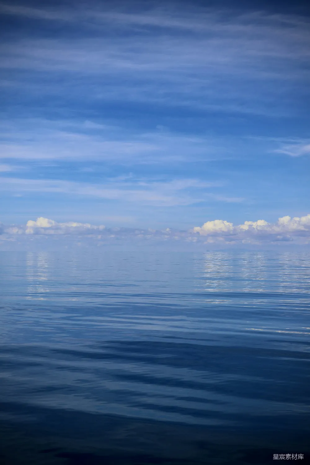 这张图片展示了一片宁静的海面与天空的完美结合。海面波光粼粼，天空中散布着几朵白云，给人一种宁静祥和的感觉。这样的场景适合用于放松心情、冥想或作为自然风光的背景。