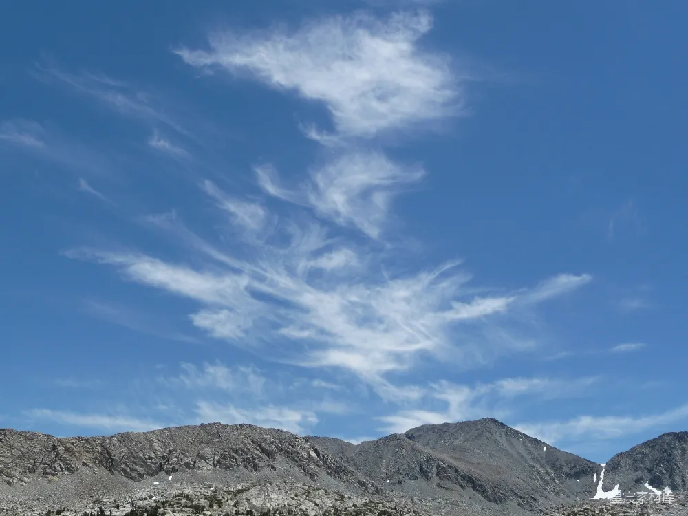 这张图片展示了蓝天下的山景，天空中飘着几朵白云，山峰裸露，岩石裸露，给人一种宁静和开阔的感觉。适合用于自然风光、户外旅行等主题的背景图片。