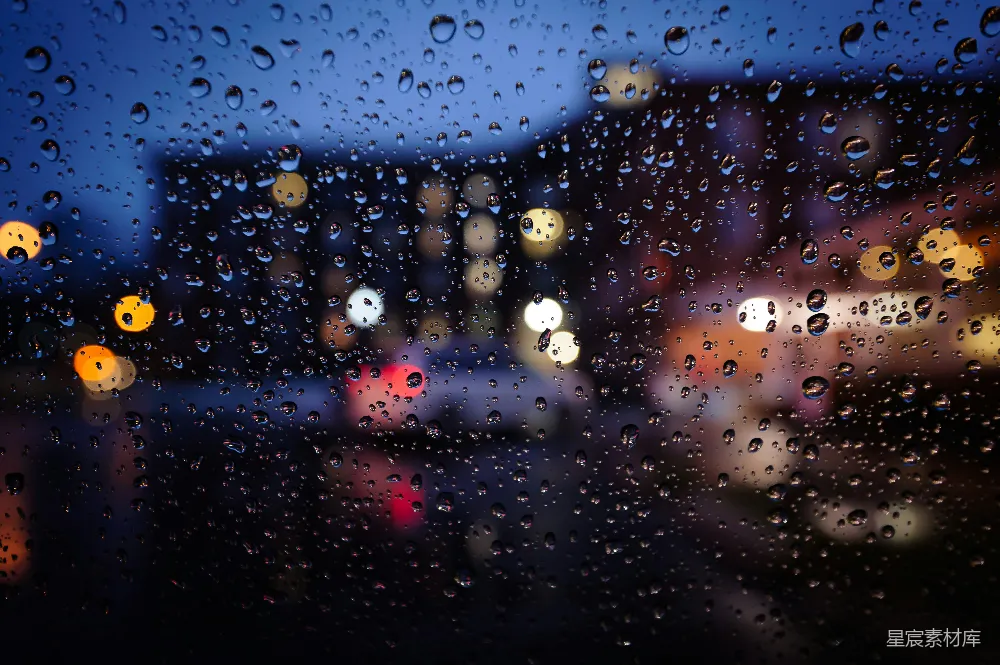 这张图片展示了夜晚城市中透过雨滴覆盖的车窗看到的景象。模糊的灯光和雨滴的反光营造出一种宁静而略带忧郁的氛围。适合用作雨天城市夜景的背景或心情描述。