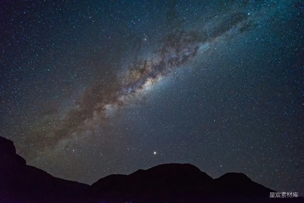 这张图片展示了夜空中璀璨的星河和山峦的剪影。银河横跨天际，星点如繁星点缀，山峦在黑暗中勾勒出清晰的轮廓，营造出一种宁静而神秘的氛围。适合用作自然风光或天文爱好者的背景图。