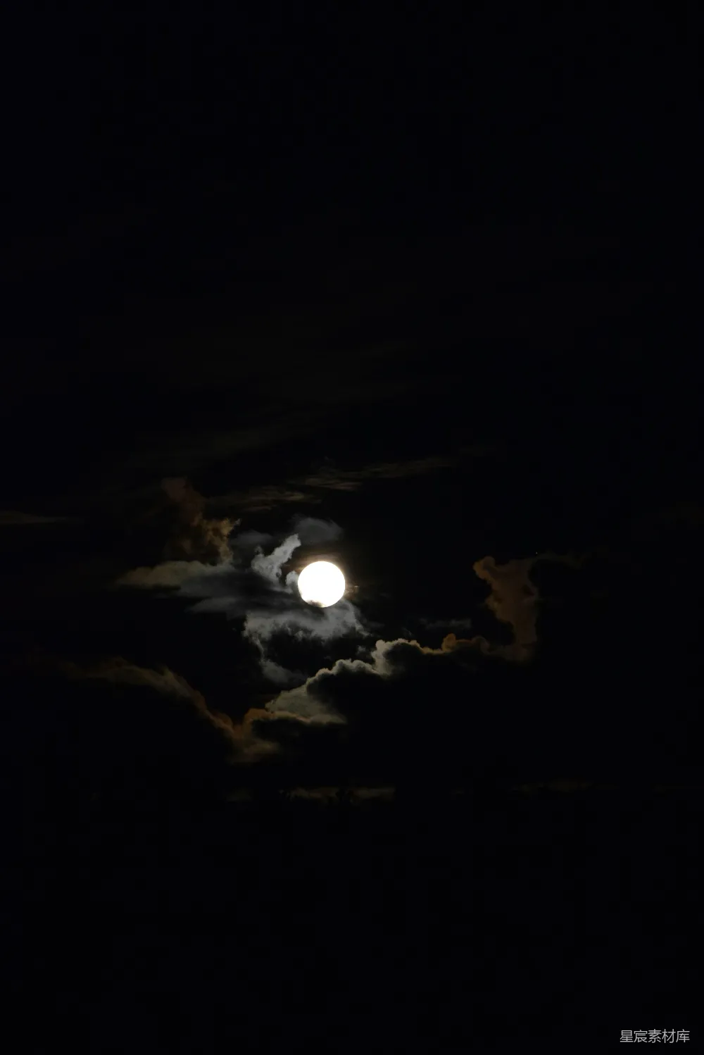 这张图片展示了一个宁静的夜晚，月亮在夜空中高悬，周围的云层被月光照亮，形成了美丽的云影。天空的深色背景与明亮的月亮形成鲜明对比，营造出一种宁静而神秘的氛围。这张图片适合用作夜景、自然风光等主题的素材。