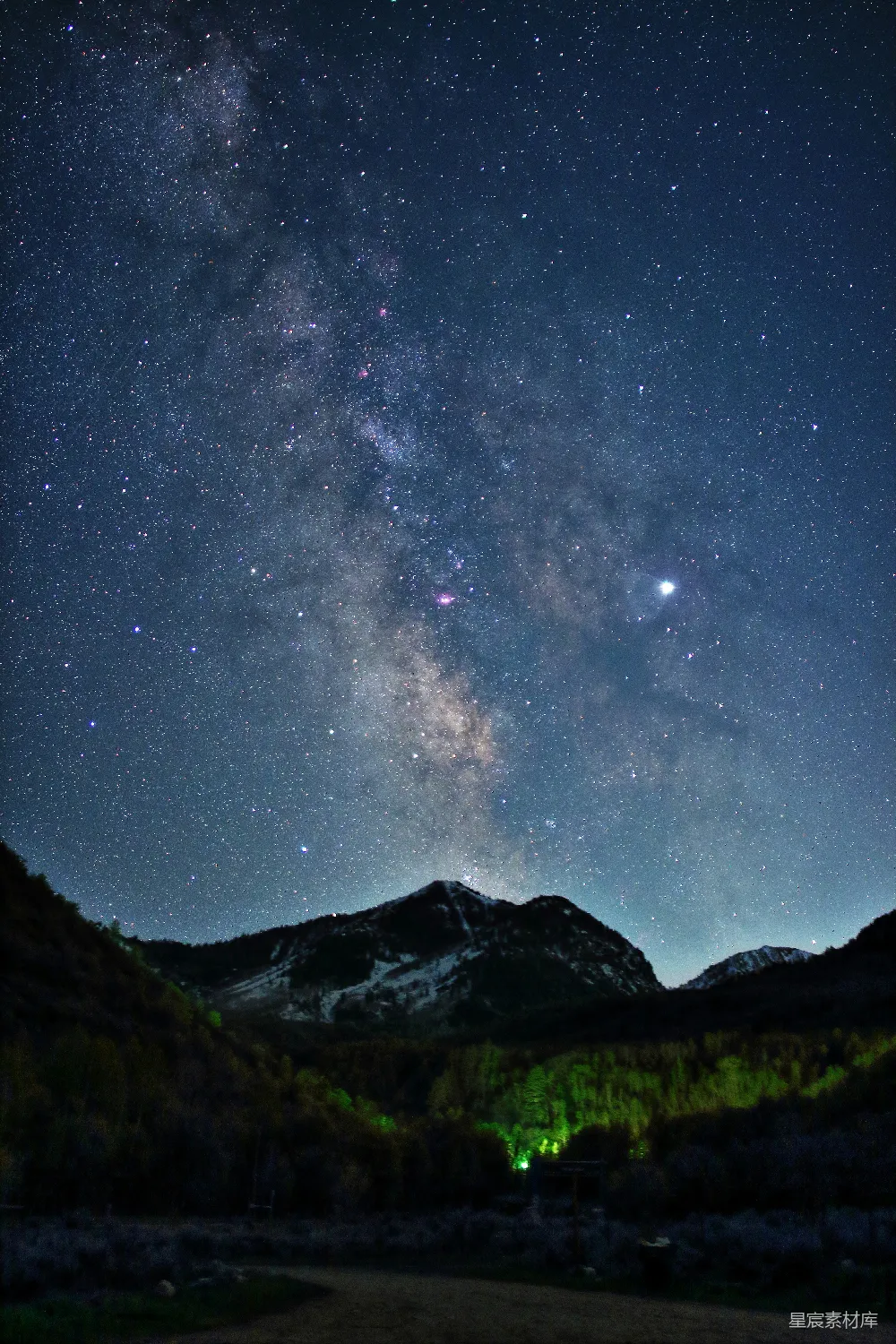 图片展示了一幅美丽的夜景，银河横跨天际，繁星点点。山峦在星光的映衬下显得宁静而神秘，地面上的植被在微弱的光线下若隐若现，营造出一种宁静而祥和的氛围。适合用于自然风光、夜景摄影或户外探险主题的素材。