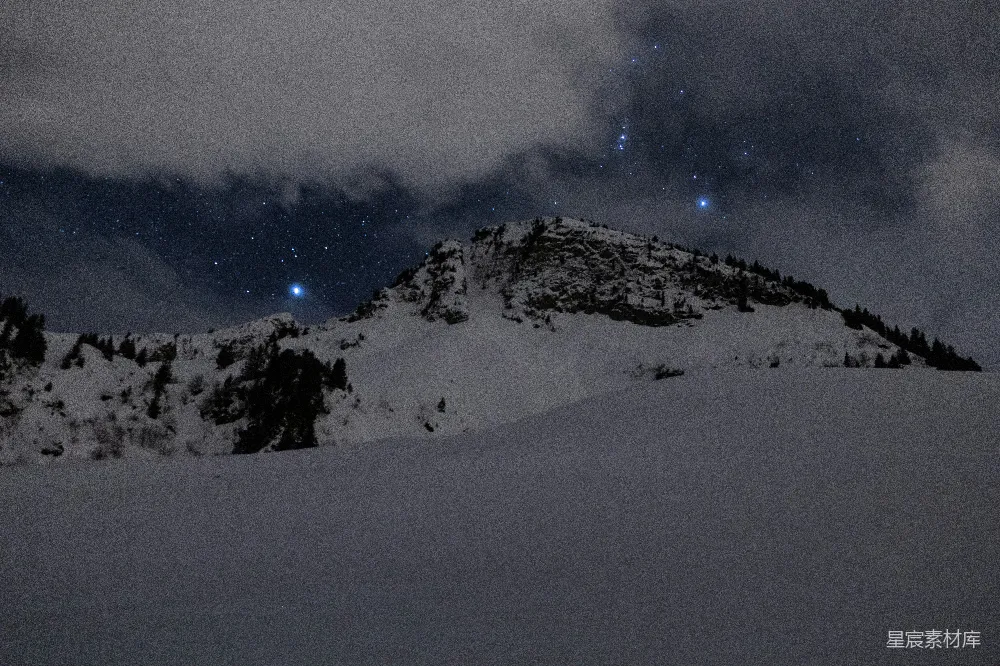 这张图片展示了一座被雪覆盖的山峰在夜色中静谧的景象。天空中星星点点，仿佛在诉说着无尽的故事。山峰的轮廓在夜色中显得格外清晰，给人一种宁静而神秘的感觉。适合用作自然风光、冬季旅行或宁静时刻的背景素材。