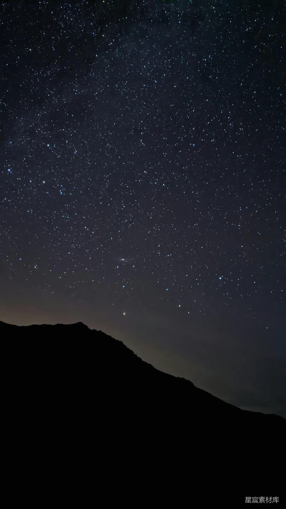 这张图片展示了宁静的夜空，满天的星星闪烁着微光，下方是黑暗的山脊轮廓，营造出一种静谧而神秘的氛围。适合用作手机壁纸或自然风光的背景。