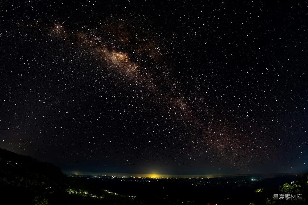这张图片展示了夜空中璀璨的星星和银河，背景是宁静的城市灯光。画面中，银河清晰可见，星星点缀其间，远处的城市灯光在黑暗中闪烁，形成了美丽的对比。这幅图像适合用作自然风光、夜景和城市生活的背景。