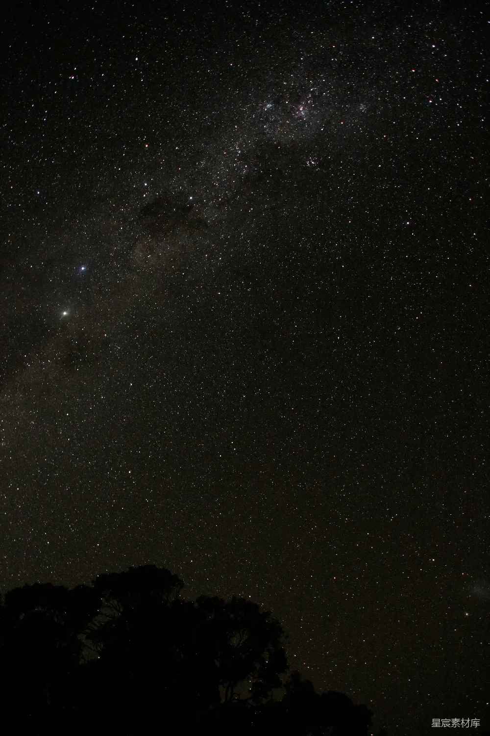 这张图片捕捉到了一个宁静的夜空，银河横跨天空，繁星点缀其间，下方是黑影般的树木轮廓，营造出一种宁静而神秘的氛围。适合用于自然风光、天文摄影或宁静氛围的场景。
