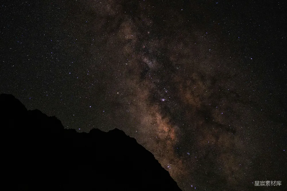 这张图片展示了一片璀璨的星河景象，银河从画面的中央延伸出来，散布着无数的星星。山峦的轮廓在前景中若隐若现，与背景的星河形成了鲜明的对比。整体画面充满了宁静与神秘的氛围，适合用作自然风光、天文摄影等场景的背景素材。
