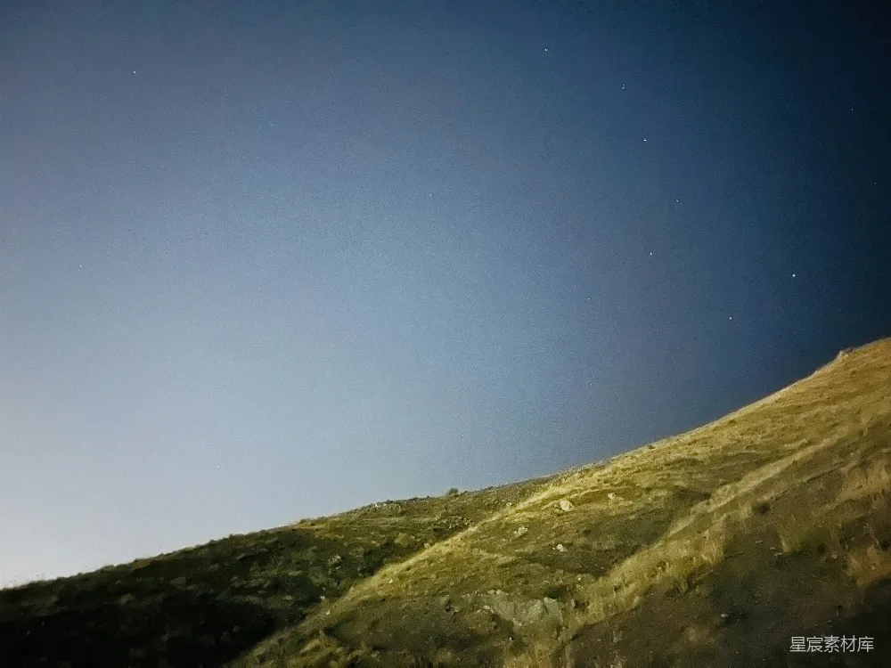 这张图片展示了一个宁静的夜晚场景，山丘上覆盖着稀疏的植被，天空中点缀着星星。画面给人一种宁静和神秘的感觉，适合用作自然风光或旅行摄影的素材。