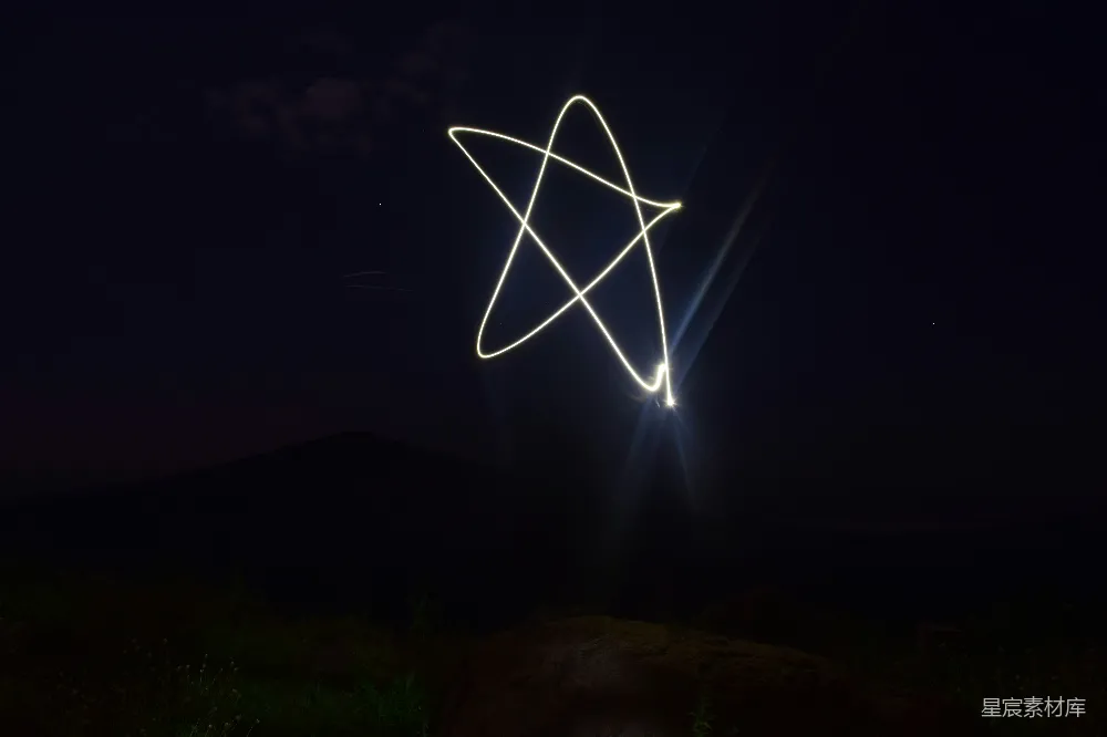 这张图片展示了夜空中由光绘技术绘制出的星形轨迹，背景是深邃的夜空和远处的山丘轮廓。光绘技术通过长时间曝光捕捉光的运动轨迹，创造出独特的视觉效果。这种场景适合用于自然风光、户外活动或艺术创作的背景。