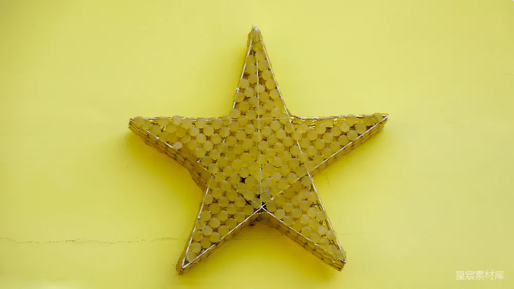 这张图片展示了一个由金色珠子组成的星星形状装饰品，背景为明亮的黄色。这个星星装饰品可能用于节日装饰、派对布置或作为家居装饰品，其简洁而精致的设计适合多种场合。