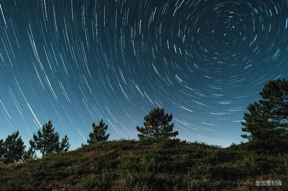 这张图片展示了夜空中星轨的美丽景象，星星的轨迹在夜空中形成了一个美丽的圆圈，下方是一片绿色的草地和几棵松树。这张图片给人一种宁静和神秘的感觉，适合用作自然风光、夜景摄影、星空摄影等场景的背景。