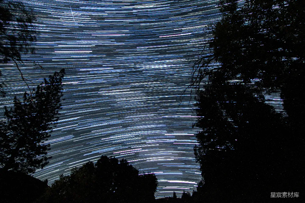 这张图片展示了夜空中的星轨，星星的轨迹在夜空中形成了一幅美丽的图案。树的剪影为画面增添了深度，背景的星轨则营造出一种宁静而神秘的氛围。适合用于自然风光、天文摄影和宁静的夜景主题。