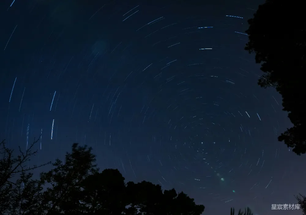 这张图片展示了夜空中星轨的美丽景象，星轨呈现出旋转的轨迹，中心是北极星，周围是星轨形成的线条，背景是深邃的夜空。树影在画面下方，增加了画面的层次感。这幅作品适合用于天文摄影、自然风光以及夜景摄影的素材库。