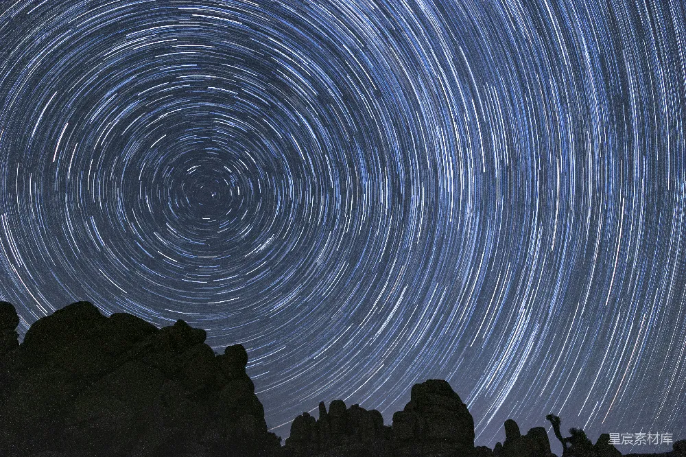 这张图片展示了夜晚天空中星轨的美丽景象，星轨呈现出螺旋状的旋转轨迹，背景是黑暗的夜空与岩石的剪影，营造出一种神秘而宁静的氛围。适合用于天文摄影爱好者、自然风光展示以及宇宙主题的背景素材。