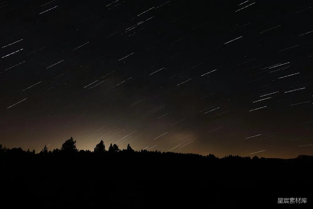 这张图片展示了夜空中星轨的美丽景象，星星在夜空中划出长长的轨迹，背景是深邃的夜空和稀疏的树木剪影，营造出一种宁静而神秘的氛围。适合用于展示自然之美，或者与天文、摄影相关的内容。